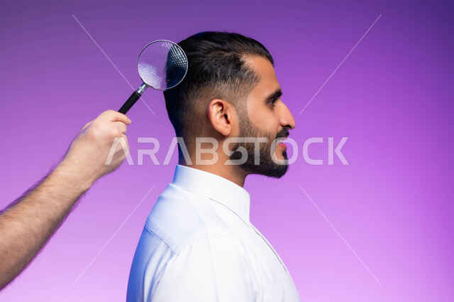 فحص فروة الرأس، سلامة الشعر من القشره والقمل، المحفاظه على النظافه والمظهر الخارجي، بورتريه مقرب ليد تضع العدسه المكبره على رأس شاب عربي سعودي خليجي يقف باستقامه، خلفية ملونة