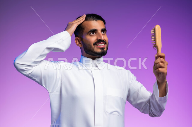 مفهوم العناية والاهتمام بالجمال والأناقة والمظهر الخارجي، بورتريه مقرب لرجل عربي خليجي سعودي يقوم بتصفيف شعره باستخدام فرشاة الشعر ( المشط )، تعابير وإيماءات تدل على السعادة والسرور، خلفية ملونة
