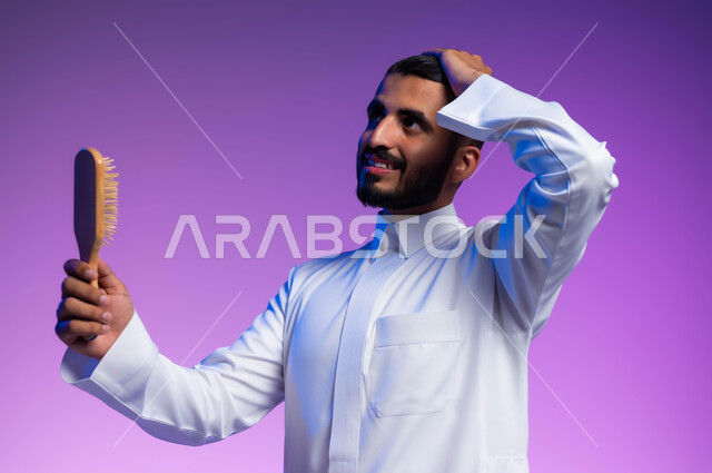 ترتيب وتمشيط الشعر، مفهوم العناية والاهتمام بالجمال والأناقة والمظهر الخارجي، بورتريه مقرب لرجل عربي خليجي سعودي يقوم بتصفيف شعره باستخدام فرشاة الشعر ( المشط ) بتعابير وإيماءات تدل على السعادة والسرور، خلفية ملونة