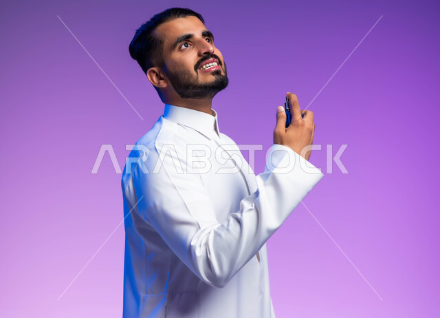 التسويق لمنتجات العطور, مفهوم التعطر والتطيب, استخدام الزيوت العطرية الطبيعية, عطورات خليجية سعودية, بورتريه مقرب من الجانب لرجل عربي خليجي سعودي يرتدي الثوب التقليدي يقوم برش العطر, خلفية ملونة
