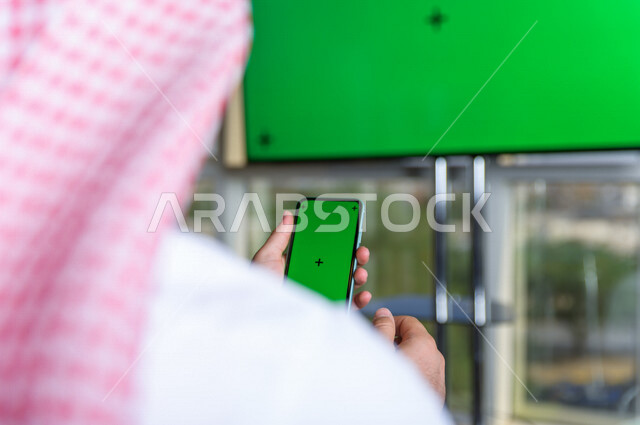 رجل أعمال سعودي خليجي يستخدام هاتفه المحمول بخلفية خضراء كروما  ، تقنية و حاسب ، استخدام تقنية السمارت على الهاتف المحمول ليتحكم بالتلفاز
