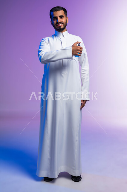 عطورات خليجية سعودية, مفهوم الاناقة والاهتمام بالمظهر الخارجي, استخدام الزيوت العطرية الطبيعية, بورتريه لرجل عربي خليجي سعودي يرتدي الثوب التقليدي يقوم بوضع العطر, التسويق لمنتجات العطور, صورة الجسم بالكامل, خلفية ملونة