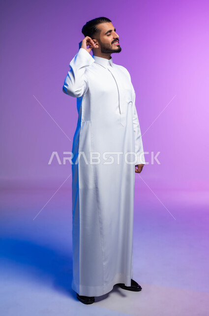 استخدام أعواد ونكاشات القطن، روتين نظافة الأذنين اليومية، بورتريه لرجل عربي خليجي سعودي يقوم بتنظيف أذنه بنكاشة قطنية ( مسحة قطنيه )، مفهوم العناية والاهتمام بصحة ونظافة الأذن، صورة الجسم بالكامل، خلفية ملونة