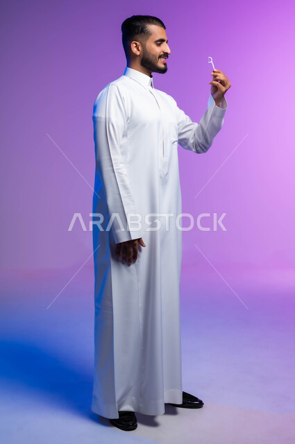 التأكد من نظافة الأسنان بعد تناول الطعام، الاهتمام بالأناقة والمظهر الخارجي، المحافظة على ابتسامة بيضاء، بورتريه من الجانب لرجل عربي خليجي سعودي يقوم بتنظيف أسنانه باستخدام الخيط السني، مفهوم العناية بصحة الفم، صورة الجسم بالكامل، خلفية ملونة