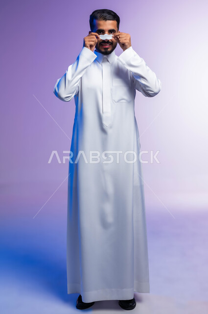 التخلص من الرؤوس السوداء والجلد الميت، استخدام ماسكات تنظيف المسام ومكونات تجميلية، بورتريه لرجل عربي خليجي سعودي يرتدي الثوب التقليدي يضع لصقات الأنف، مفهوم العناية والاهتمام بنضارة وتحسين البشرة، صورة لكامل الجسم، خلفية ملونة