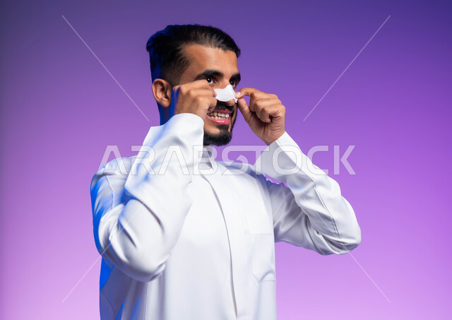 التخلص من الرؤوس السوداء والجلد الميت، استخدام ماسكات تنظيف المسام ومكونات تجميلية، بورتريه مقرب لرجل عربي خليجي سعودي يرتدي الثوب التقليدي يضع لصقات الأنف، مفهوم العناية والاهتمام بنضارة وتحسين البشرة، خلفية ملونة
