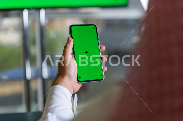 رجل أعمال سعودي خليجي يستخدام هاتفه المحمول بخلفية خضراء كروما ، تقنية و حاسب ، استخدام تقنية السمارت على الهاتف المحمول ليتحكم بالتلفاز