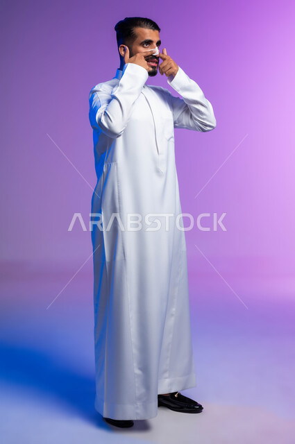 استخدام ماسكات تنظيف المسام ومكونات تجميلية، مفهوم العناية والاهتمام بنضارة وتحسين البشرة، التخلص من الرؤوس السوداء والجلد الميت، بورتريه من الجانب لرجل عربي خليجي سعودي يرتدي الثوب التقليدي يضع لصقات الأنف، صورة لكامل الجسم، خلفية ملونة