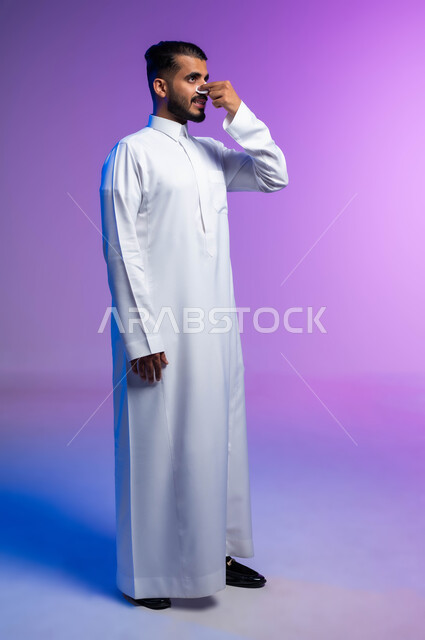 استخدام ماسكات تنظيف المسام ومكونات تجميلية، مفهوم العناية والاهتمام بنضارة وتحسين البشرة، التخلص من الرؤوس السوداء والجلد الميت، بورتريه من الجانب لرجل عربي خليجي سعودي يرتدي الثوب التقليدي يضع لصقات الأنف، صورة لكامل الجسم، خلفية ملونة