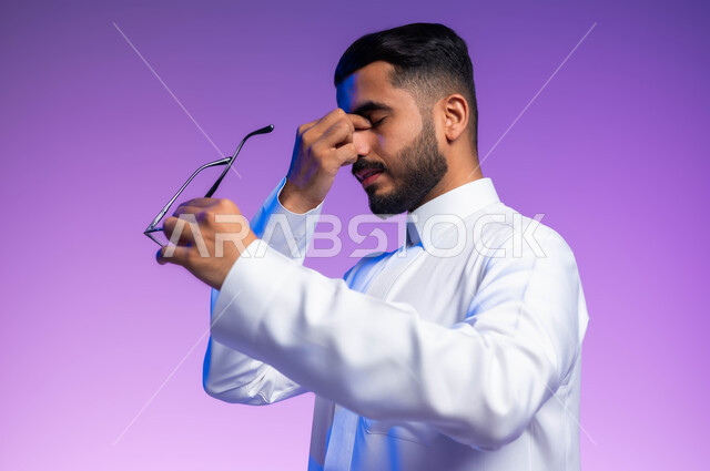 ارتداء النظارات الخاصة بضعف النظر، الاناقة والاهتمام بالمظهر الخارجي، بورتريه مقرب من الجانب لرجل عربي خليجي سعودي يرتدي الثوب التقليدي يمسك النظاره الطبيه يضع يده على وجهه بإيماءات التعب والإرهاق، مفهوم تعديل وتحسين الرؤية، خلفية ملونة