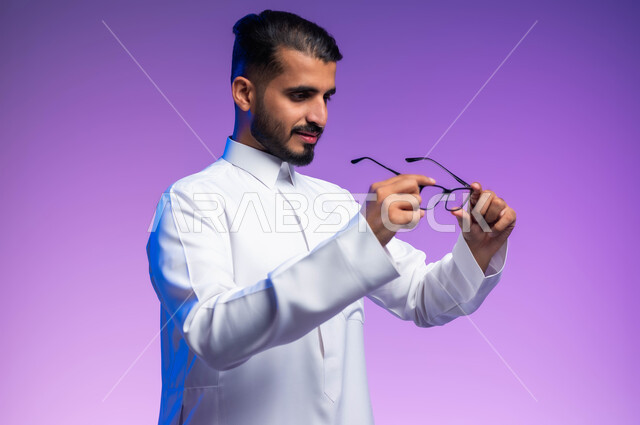 ارتداء النظارات الخاصة بضعف و قصر النظر، الاناقة والاهتمام بالمظهر الخارجي، بورتريه مقرب من الجانب لرجل عربي خليجي سعودي يرتدي الثوب التقليدي يمسك بيده نظاره طبيه، مفهوم تحسين الرؤية ومحاولة تعديل البصر، خلفية ملونة