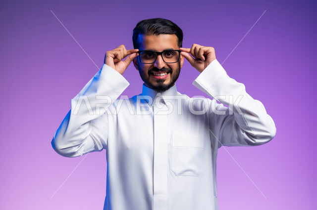 الاناقة والاهتمام بالمظهر الخارجي، بورتريه مقرب لرجل عربي خليجي سعودي مبتسم يرتدي الثوب التقليدي يمسك بيده نظاره طبيه ينظر إلى الكاميرا بإيماءات السرور والسعادة، ارتداء النظارات الخاصة بضعف النظر، مفهوم تحسين الرؤية ومحاولة تعديل البصر، خلفية ملونة