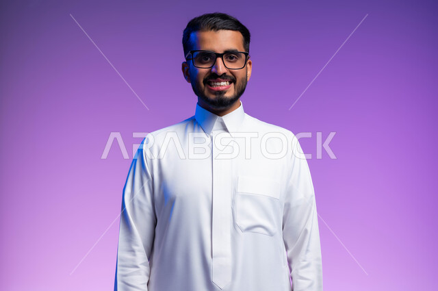 Wearing glasses for low vision, a close-up portrait of a smiling Saudi Arabian Gulf man wearing a traditional thobe, wearing medical glasses, looking at the camera with gestures of pleasure and happiness, taking care of external appearance, the concept of improving vision and trying to correct eyesight, a colored background.