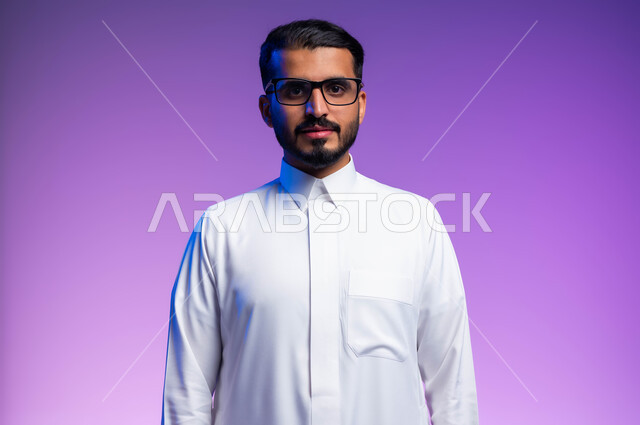The concept of improving vision and trying to modify eyesight, paying attention to external appearance, wearing glasses for low vision, a close-up portrait of a Saudi Gulf Arab man wearing a traditional dress, wearing medical glasses, looking at the camera with frowning gestures, a colored background.