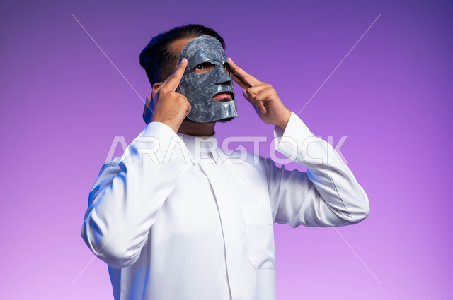خطوات تنظيف وتقشير البشرة، بورتريه مقرب لرجل عربي خليجي سعودي يقوم بوضع قناع الطين على وجهه، مفهوم العناية والاهتمام بالمظهر الخارجي، استخدام مكونات تجميلية، خلفية بيضاء.