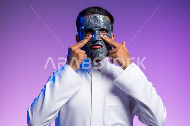 استخدام مكونات تجميلية، خطوات تنظيف وتقشير البشرة، بورتريه مقرب لرجل عربي خليجي سعودي يقوم بوضع قناع الطين على وجهه، مفهوم العناية والاهتمام بالمظهر الخارجي، خلفية بيضاء.