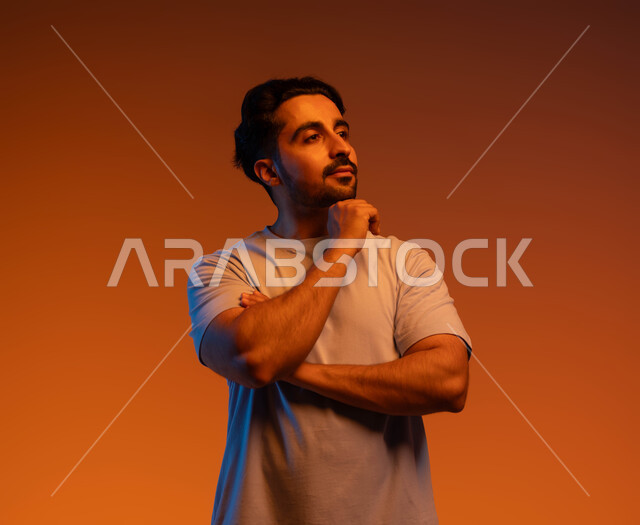 Finding a solution to a problem, the concept of concentration, absent-mindedness, and contemplation, a close-up portrait of a Saudi Gulf Arab man wearing casual clothes, placing his hand on his chin and looking at something with gestures of thinking, contemplation, and planning for the future, colorful background