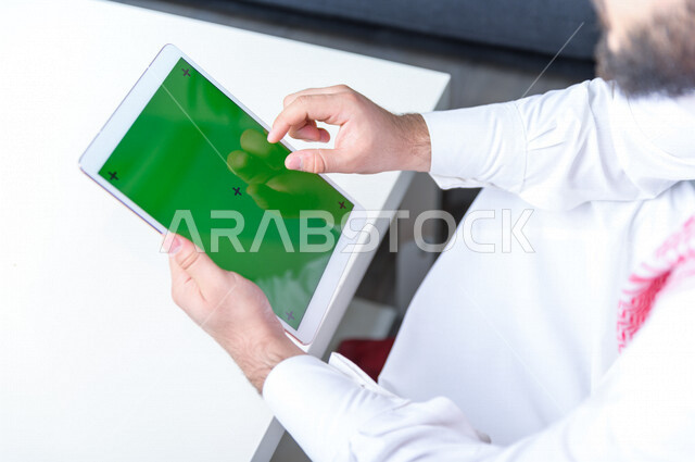رجل أعمال سعودي خليجي يستخدام جهاز لوحي تابلت بشاشة خضراء كروما ، تقنية و حاسب ، شراء عن بعد ، التعليم عن بعد ، العاب فيديو