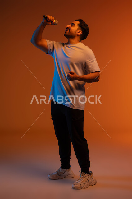 Gestures indicating integration and interaction with singing, recording a singing audio clip, spending an enjoyable time performing vocal performances, a portrait of a Saudi Gulf Arab young man wearing a casual outfit holding a microphone in his hand and singing enthusiastically, practicing artistic talents, a full-body portrait, a colorful background.
