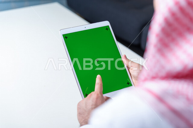 رجل أعمال سعودي خليجي يستخدام جهاز لوحي تابلت بشاشة خضراء كروما ، تقنية و حاسب ، شراء عن بعد ، التعليم عن بعد ، العاب فيديو