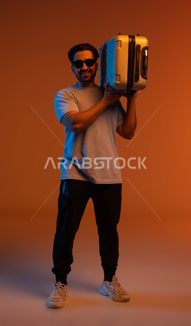Tourist activities and events, looking at the camera with expressions of joy and pleasure, going on recreational tours during the summer vacation, a portrait of a Saudi Gulf Arab young man wearing a casual outfit and sunglasses carrying a travel bag on his shoulder, preparing for an enjoyable summer trip, a full-body portrait, a colorful background