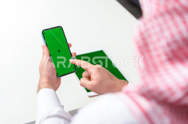 رجل أعمال سعودي خليجي يستخدام هاتفه المحمول بخلفية خضراء كروما ، تقنية و حاسب ، استخدام تقنية السمارت على الهاتف المحمول ليتحكم بالتلفاز