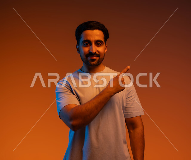 الإشارة إلى هدف محدد, الوقوف والنظر إلى الكاميرا, بورتريه مقرب لشاب عربي خليجي سعودي يرتدي الزي الكاجوال يرفع اصبعه لتحديد وتوضيح موقع معين, الذهاب لمكان ما, خلفية ملونة