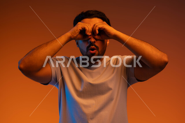 التخطيط للأهداف والطموحات المستقبلية, الوقوف باندهاش واستغراب, رؤية الأشياء البعيدة, بورتريه لشاب عربي خليجي سعودي يرتدي الزي الكاجوال يضع يديه على عينيه بشكل عدسة, حب الاكتشاف والمعرفة والمغامرة, خلفية ملونة