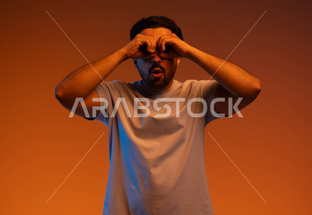 الوقوف باندهاش واستغراب, رؤية الأشياء البعيدة, التخطيط للأهداف والطموحات المستقبلية, بورتريه لشاب عربي خليجي سعودي يرتدي الزي الكاجوال يضع يديه على عينيه بشكل عدسة, حب الاكتشاف والمعرفة والمغامرة, خلفية ملونة