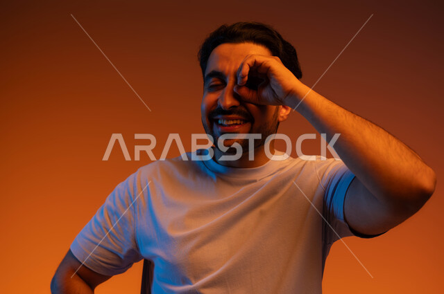 التخطيط والرؤية المستقبلية للأهداف والطموحات, بورتريه مقرب لشاب عربي خليجي سعودي مبتسم يرتدي الزي الكاجوال يضع يديه على عينه على شكل عدسة, حب المعرفة والاكتشاف والمغامرة, رؤية الأشياء عن قرب, خلفية ملونة