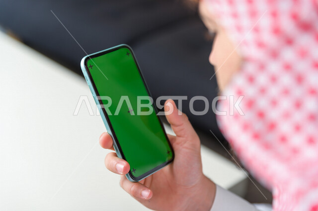 A Saudi Gulf businessman uses his mobile phone with a green background, chroma, technology and computer, using smart technology on the mobile phone to control the TV