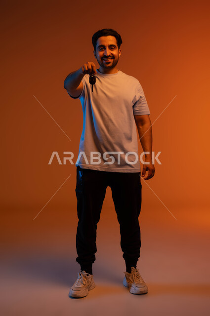 الحصول على رخصة قيادة, خدمة صف السيارة بالمواقف الخاصة, اقتناء سيارة جديدة بإيماءات السرور, بورتريه لشاب عربي خليجي سعودي مبتسم يرتدي الزي الكاجوال يمسك بيده مفتاح السيارة, استلام وتسليم المفاتيح, صورة الجسم بالطول الكامل, خلفية ملونة