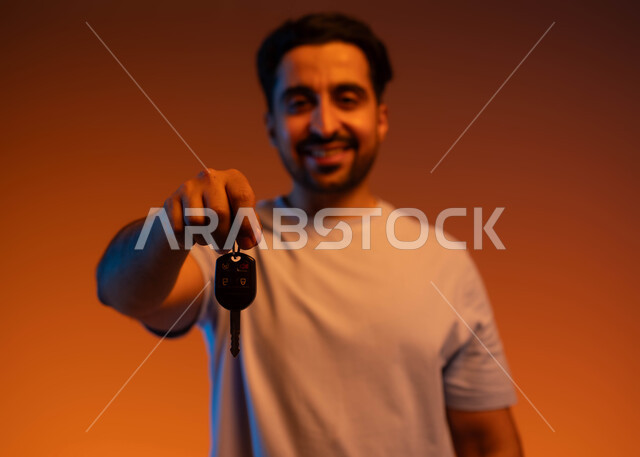 اقتناء سيارة جديدة بإيماءات السرور, الحصول على رخصة قيادة, بورتريه مقرب لشاب عربي خليجي سعودي مبتسم يرتدي الزي الكاجوال يمسك بيده مفتاح السيارة وينظر إلى الكاميرا, خدمة صف السيارة بالمواقف الخاصة, استلام وتسليم المفاتيح, خلفية ملونة