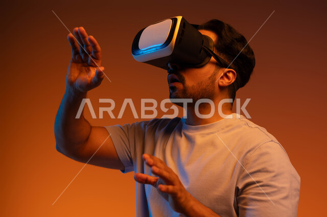 Using advanced technologies and devices, a close-up portrait of a young Saudi Arab Gulf man wearing casual clothes and 3D virtual reality glasses, the concept of interaction and integration, fun and entertainment by watching movies and simulating the imaginary world, a colorful background
