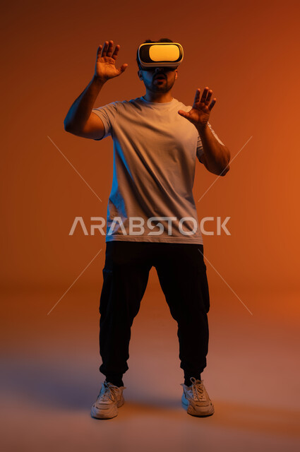 The concept of interaction and integration, the use of advanced technologies and devices, a portrait of a young Saudi Arab Gulf man wearing casual clothes and 3D virtual reality glasses trying to touch something, having fun watching movies and simulating the imaginary world, full-length body image, colored background