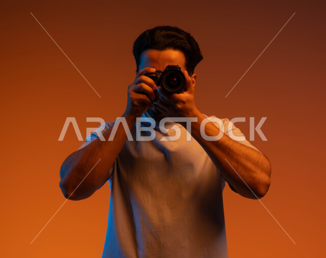 A professional photographer takes souvenir photos, practicing the hobby of photography, a close-up portrait of a Saudi Gulf Arab young man wearing a casual outfit, holding a photographic camera in his hand, using high-resolution digital cameras, colored background