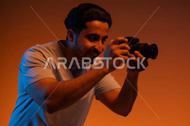 Using high-resolution digital cameras, practicing the hobby of photography, a professional photographer taking souvenir photos, Saudi jobs and professions, a close-up portrait of a Saudi Gulf Arab man wearing a casual outfit, taking photos with a photographic camera, colored background