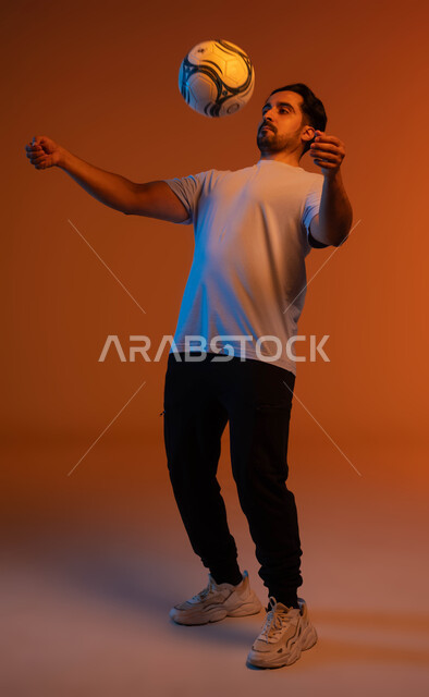 فنون ومهارات اللعب، المحافظة على اللياقة البدنية أنثاء ممارسة الهواية المفضلة، بورتريه للاعب عربي سعودي خليجي يرتدي الزي الكاجوال يلعب بكرة القدم، التسلية و الترفيه بالرياضات الحركية، صورة الجسم بالكامل، خلفية ملونة