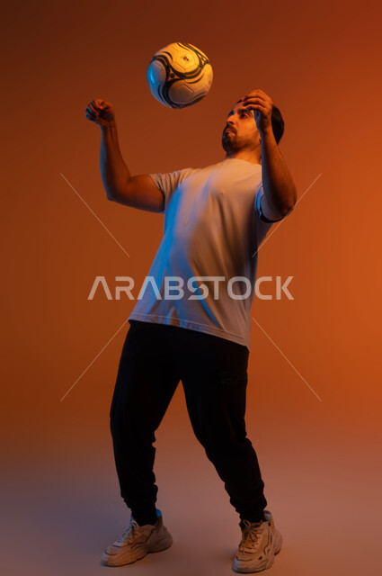 المحافظة على اللياقة البدنية أنثاء ممارسة الهواية المفضلة، فنون ومهارات اللعب، بورتريه للاعب عربي سعودي خليجي يرتدي الزي الكاجوال يلعب بكرة القدم، التسلية و الترفيه بالرياضات الحركية، صورة الجسم بالكامل، خلفية ملونة