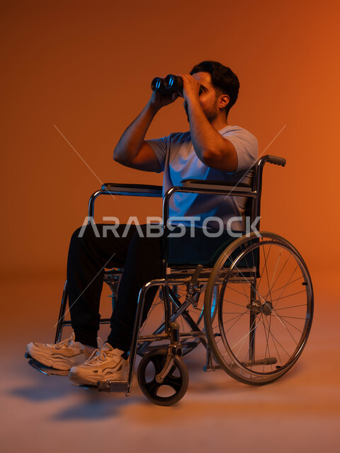 رؤية مستقبلية عند أصحاب ذوي الهمم، حب الاستكشاف والمغامرة ،بورتريه لرجل عربي خليجي سعودي مقعد يرتدي الزي الكاجوال يجلس على كرسي متحرك و يحمل بيده المنظار ثنائي العينين، التخطيط المستقبلي للأهداف والطموحات ،خلفية ملونة .