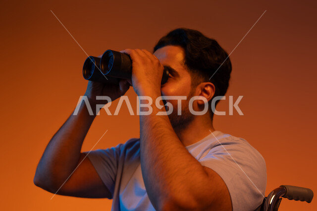 التخطيط المستقبلي للأهداف والطموحات ، رؤية مستقبلية عند أصحاب ذوي الهمم، بورتريه مقرب لرجل عربي خليجي سعودي مقعد يرتدي الزي الكاجوال يجلس على كرسي متحرك و يحمل بيده المنظار ثنائي العينين، حب الاستكشاف والمغامرة ، خلفية ملونة .