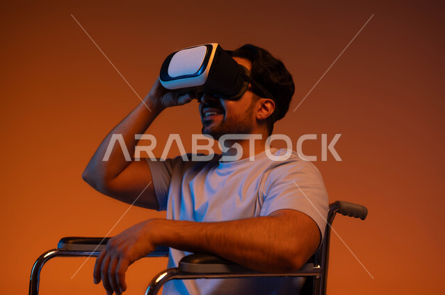 استخدام التقنيات المتطورة الحديثة لتحسين حياة أصحاب الهمم وتأمين احتياجاتهم الخاصة، بورتريه مقرب لشاب عربي خليجي سعودي مبتسم مقعد يجلس على كرسي متحرك و يرتدي نظارة الواقع الافتراضي، خلفيه ملونة .