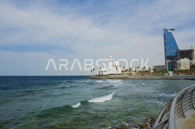 النمو والتطور العمراني ،أشجار النخيل الخضراء على الواجهة البحرية، اماكن اسلامية دينية مقدسة ،أمواج البحر الهادئة على الشاطئ، الفن الهندسي المعماري للمعالم سياحية مشهورة في السعودية على كورنيش مدينة جدة