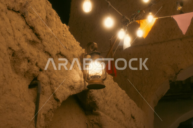 فانوس معدني عربي مضيئ معلق على الجدران المبنية من الطين، زينة وديكورات شهر الخير والبركة ،الاستعداد لاستقبال شهر رمضان المبارك، العبادة والتقرب الى الله تعالى