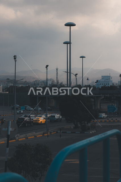منظر الغيوم الملبدة في السماء، أعمدة الانارة في شوارع سلطنة عمان، الحركة المرورية للسيارات في الطرقات المعبدة، وسائل النقل والمواصلات