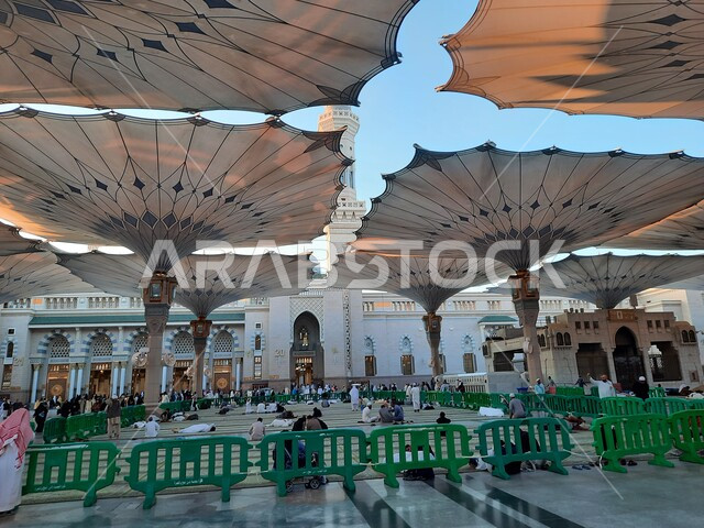ساحة المسجد النبوي في المدينة المنورة، الحرم النبوي الشريف في وضح النهار، أماكن ومعالم دينية إسلامية مقدسة في المملكة العربية السعودية، تجمع المسلمون لأداء فروض الصلوات والعبادة والتقرب الى الله، المظلات الإلكترونية للتظلل والحماية