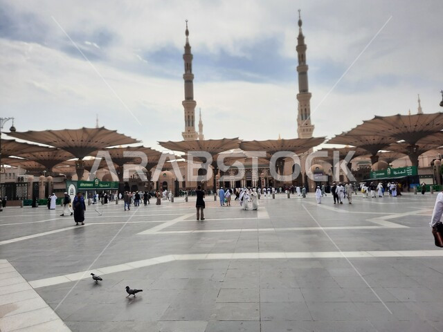 The outer courtyard of the Prophet’s Mosque in Medina, electronic awnings for shade and protection, the Prophet’s Mosque in broad daylight, sacred Islamic religious landmarks and places in the Kingdom of Saudi Arabia, Muslims gathered to perform the obligations of prayers, worship, and draw closer to God.