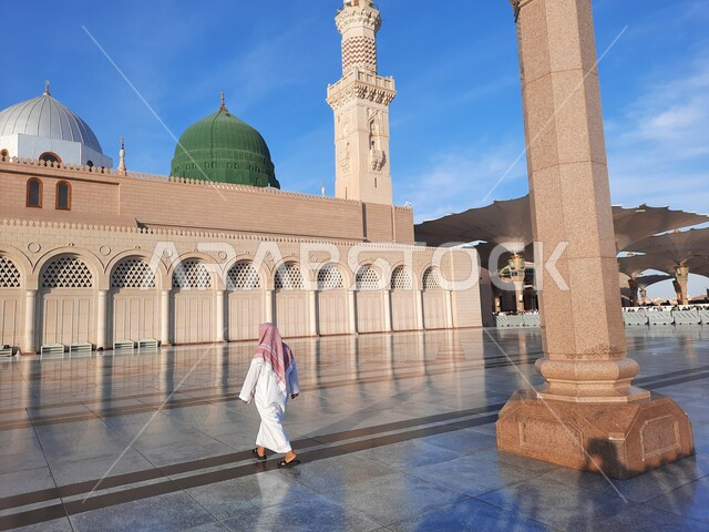 معالم دينية إسلامية، القبة الخضراء ومئذنة المسجد النبوي في المدينة المنورة بالمملكة العربية السعودية، صورة من الخلف لرجل عربي خليجي سعودي يمشي في الحرم النبوي الشريف، العبادة والتقرب الى الله