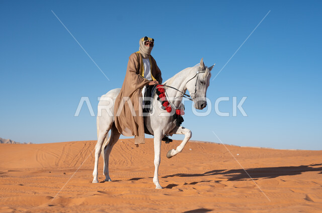 مشاركة الجياد في المناسبات والأعياد الوطنية, رجل عربي خليجي سعودي يرتدي العقال العريض والبشت التقليدي يقوم بامتطاء فرسه الابيض في وضح النهار في الصحراء, ذكرى تأسيس المملكة 22 فبراير، ارتداء أزياء أهل المنطقه الوسطى في يوم التأسيس