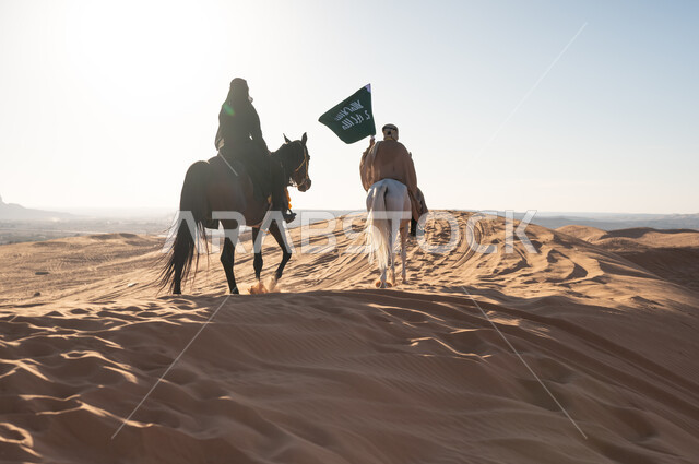 ذكرى تأسيس الدولة السعودية ١٧٢٧، قوة وأصالة الحصان العربي، الاحتفال بالمناسبات والأعياد الوطنية، فعاليات سباق الخيول العربية في الصحراء، فارسان عربيان خليجيان سعوديان يرتديان الزي التقليدي يمتطيان الجياد ويتسابقان فوق الرمال الذهبية في وضح النهار